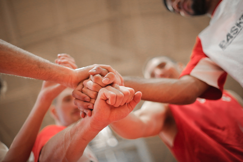 Canva - Basketball team stacking hands together 1
